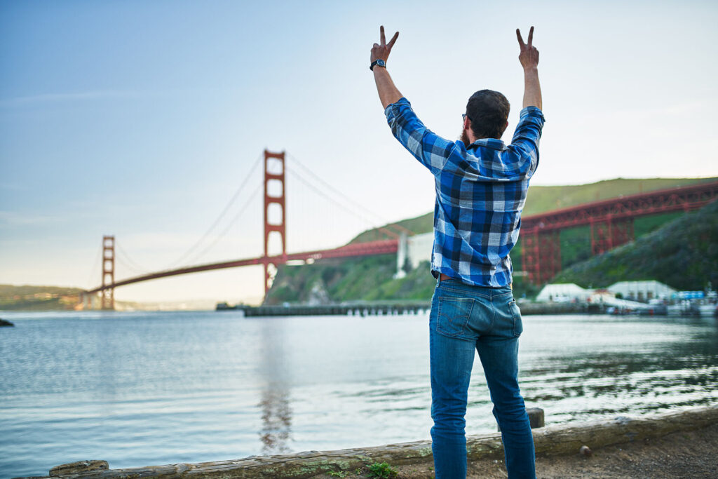 Man in recovery looking out at the San Francisco Bay while holding peace signs