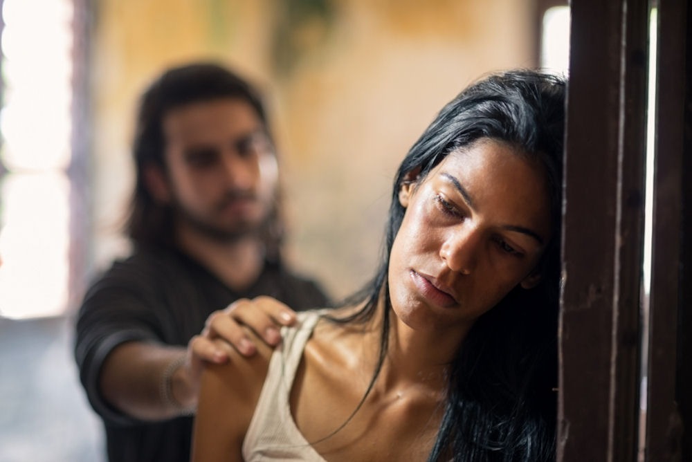 Man reaching out to despondent woman leaning on door frame