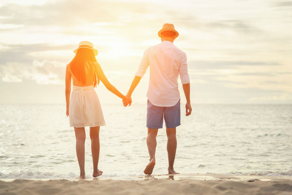 Heterosexual couple wearing Panama hats walking into the ocean holding hands