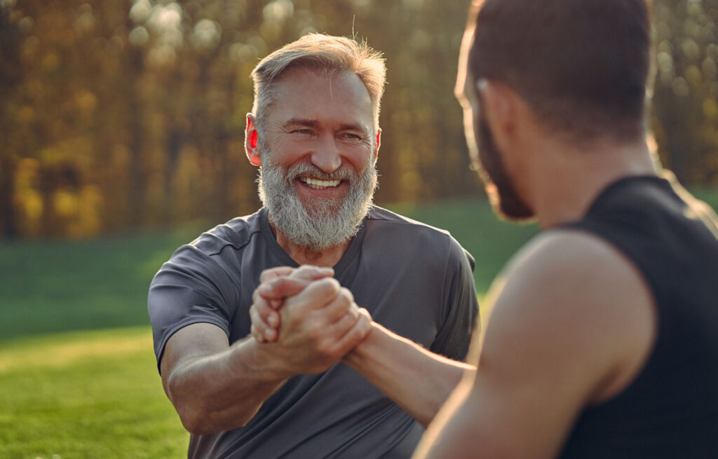 Older man and younger man happily grasping hands in solidarity