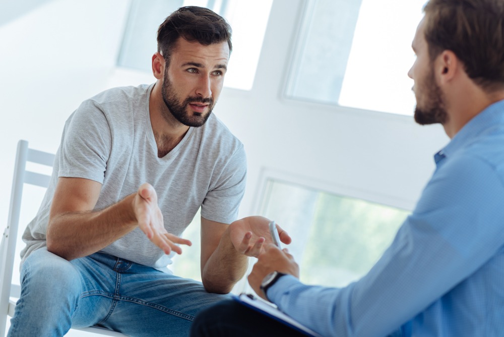 Man explaining self-medicating to therapist with clipboard