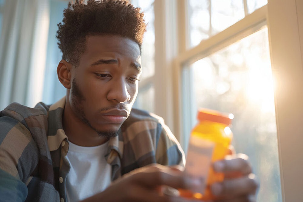 Man looking down at pill bottle while thinking about childhood trauma