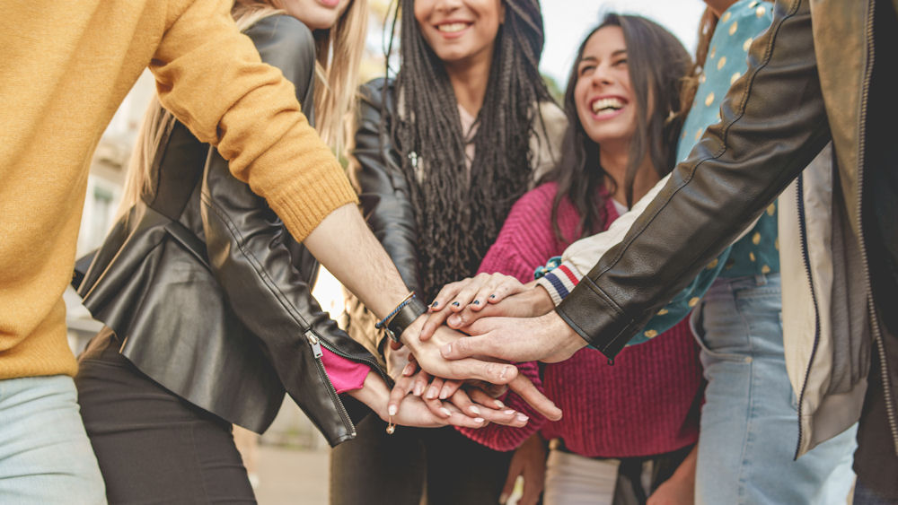 Group of women wearing different styles of outfits putting their hands together for a group cheer