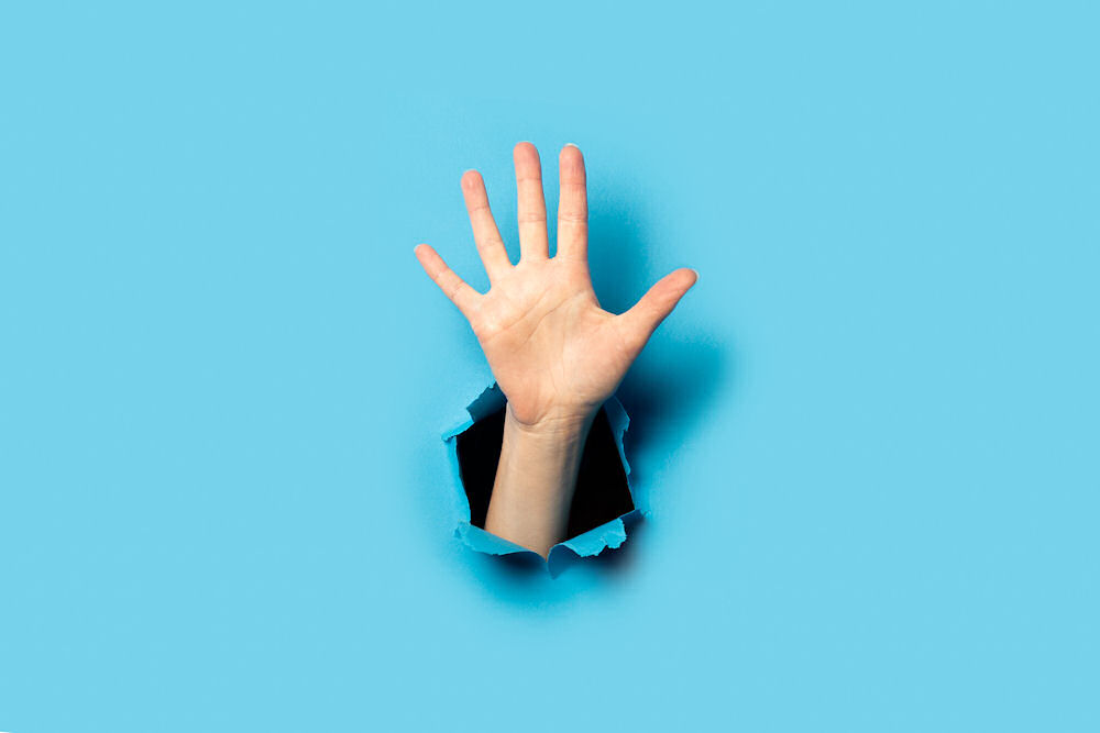 Woman's hand emerging through a torn hole in robin's egg blue wallpaper